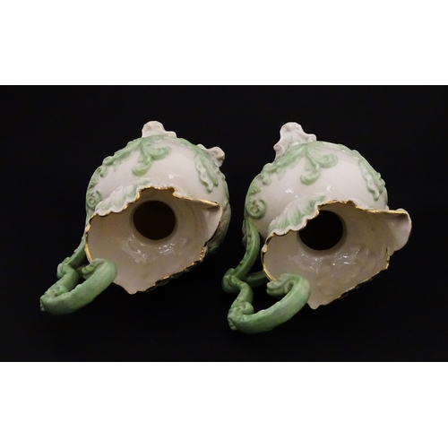 85 - A pair of Belleek jugs of shaped form with scrolling foliate decoration and green highlights. Both m... 