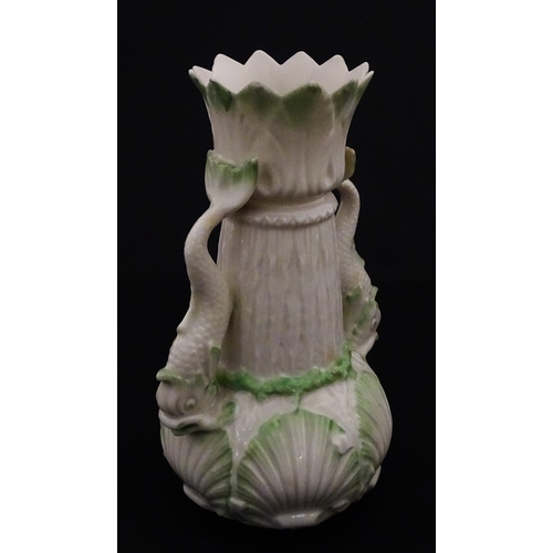 87 - A Belleek dolphin spill vase with twin fish handles and shell detail to base. Marked with Second Per... 