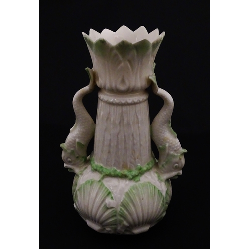 87 - A Belleek dolphin spill vase with twin fish handles and shell detail to base. Marked with Second Per... 