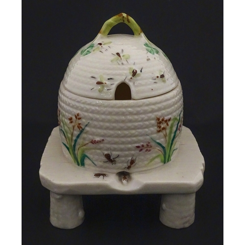 94 - A Belleek honey pot on stand of skep / beehive form decorated with bees, flowers and shamrocks. Rais... 