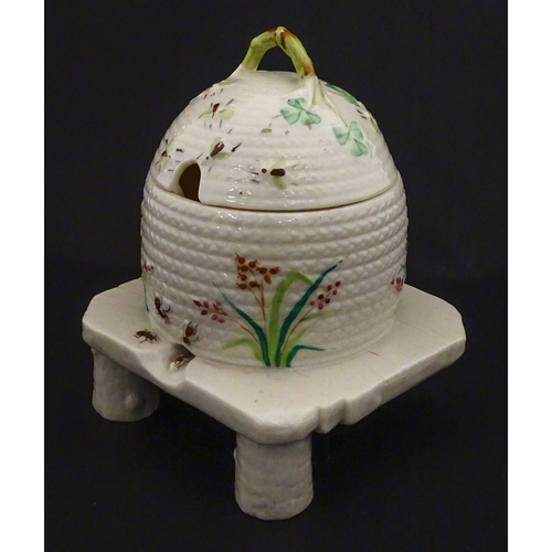 94 - A Belleek honey pot on stand of skep / beehive form decorated with bees, flowers and shamrocks. Rais... 