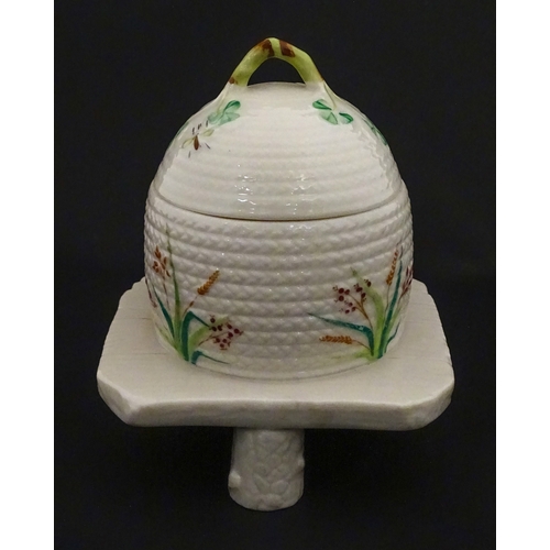 94 - A Belleek honey pot on stand of skep / beehive form decorated with bees, flowers and shamrocks. Rais... 