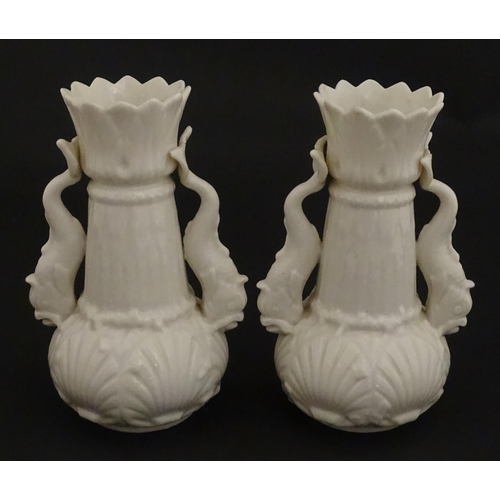 110 - A pair of Belleek dolphin spill vases with twin fish handles and shell detail to base. Marked with S... 