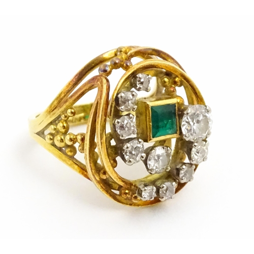 An 18ct gold Modernist ring set with square cut emerald and ten diamonds in a scrolling mount with openwork detail, hallmarked Birmingham 1977, maker Thomas Payne and Peter Trigg . Ring size approx. M