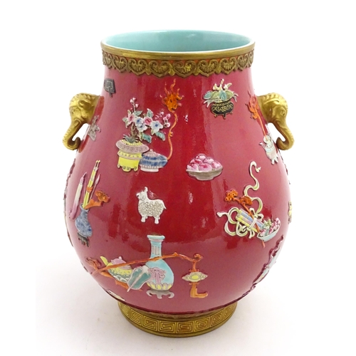 48 - A Chinese famille rose vase with twin elephant mask handles decorated in relief with vases, flowers ... 