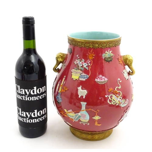 48 - A Chinese famille rose vase with twin elephant mask handles decorated in relief with vases, flowers ... 