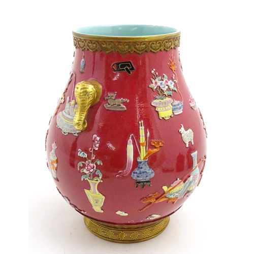 48 - A Chinese famille rose vase with twin elephant mask handles decorated in relief with vases, flowers ... 