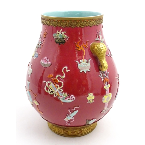 48 - A Chinese famille rose vase with twin elephant mask handles decorated in relief with vases, flowers ... 