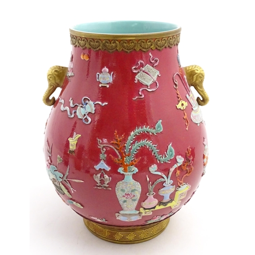 48 - A Chinese famille rose vase with twin elephant mask handles decorated in relief with vases, flowers ... 