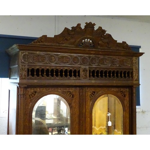 35 - A late 19thC Breton style armoire with carved floral decoration and carved masks with turned finials... 