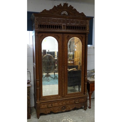 35 - A late 19thC Breton style armoire with carved floral decoration and carved masks with turned finials... 