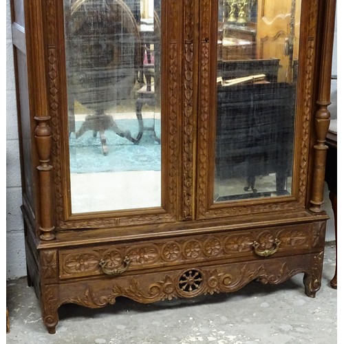 35 - A late 19thC Breton style armoire with carved floral decoration and carved masks with turned finials... 