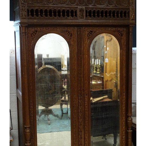 35 - A late 19thC Breton style armoire with carved floral decoration and carved masks with turned finials... 