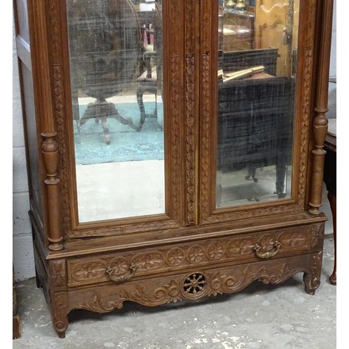 35 - A late 19thC Breton style armoire with carved floral decoration and carved masks with turned finials... 