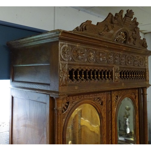 35 - A late 19thC Breton style armoire with carved floral decoration and carved masks with turned finials... 