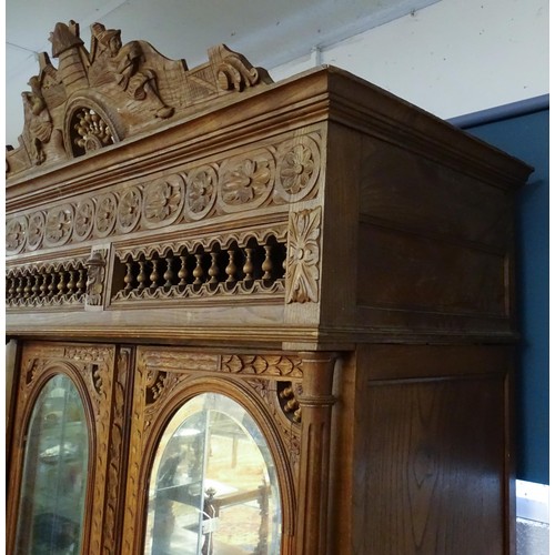 35 - A late 19thC Breton style armoire with carved floral decoration and carved masks with turned finials... 