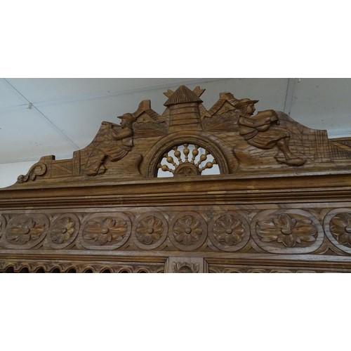 35 - A late 19thC Breton style armoire with carved floral decoration and carved masks with turned finials... 