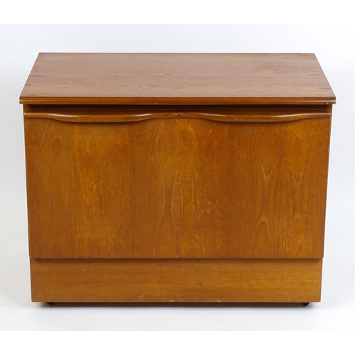 21 - Vintage / Retro: A teak two door cabinet raised on castors. 29 1/2