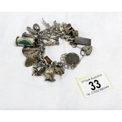 33 - A vintage silver charm bracelet with 25 charms including some opening, a heart locket etc