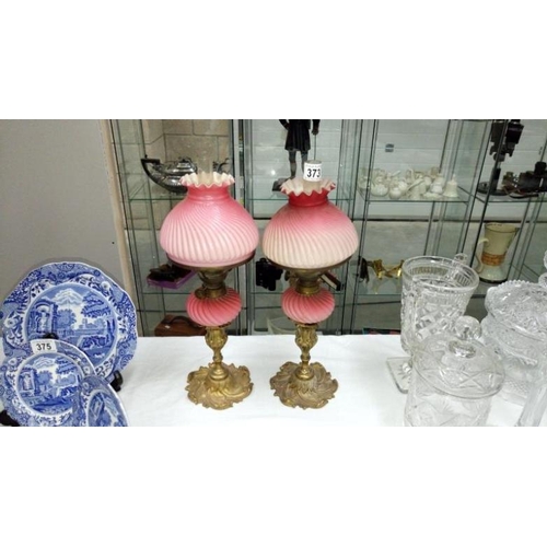 373 - A pair of pink satin glass peg font oil lamps on ormolu brass bases (1 shade chipped)