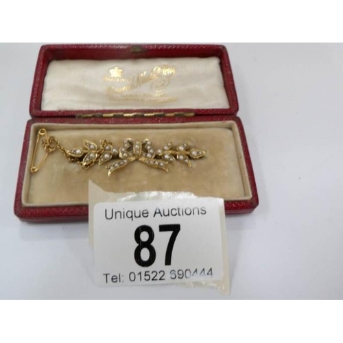 87 - An Edwardian brooch with pearls fashioned as a ribbon (tested as gold) in original box