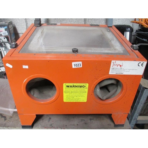 1023 - A cabinet sandblaster with various grades of blast media and a bench