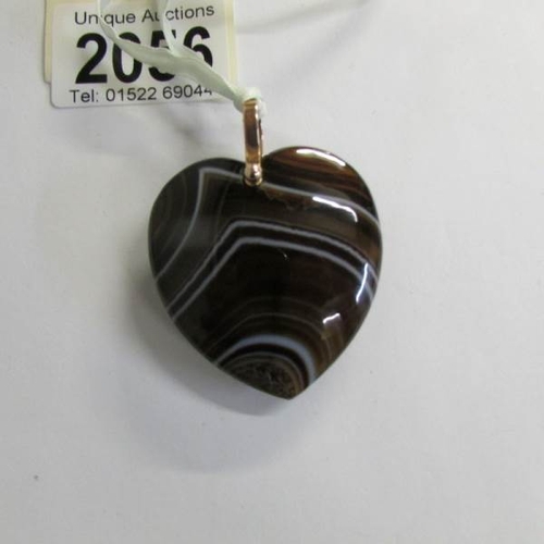 2056 - A banded agate heart shaped pendant with a rose gold 9ct loop on a silk ribbon.