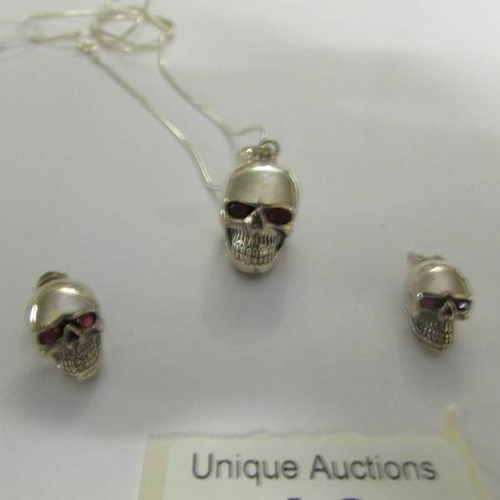 18 - A silver skull pendant and matching earrings with ruby eyes.