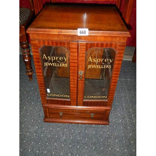 668 - A mahogany glazed two door display cabinet with drawers with Asprey's advertising glazed panels.