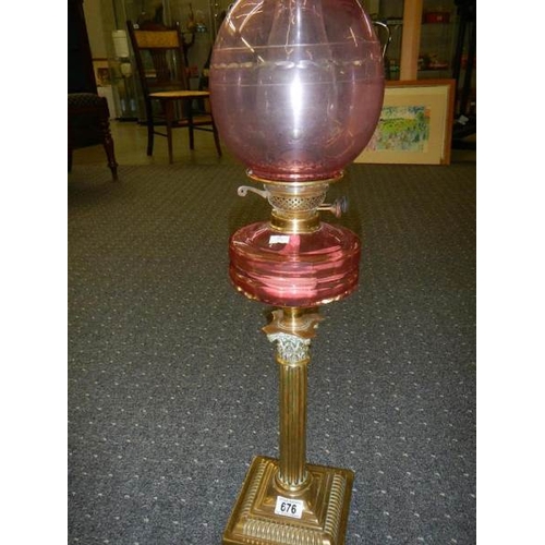 676 - A brass Corinthian column oil lamp with cranberry glass font and shade.