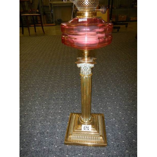 676 - A brass Corinthian column oil lamp with cranberry glass font and shade.