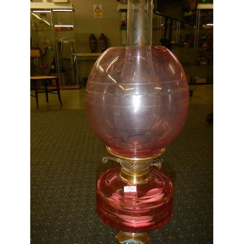 676 - A brass Corinthian column oil lamp with cranberry glass font and shade.