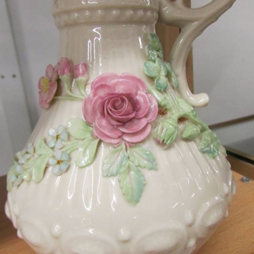 141 - A Belleek jug decorated with applied roses, 23 cm tall.