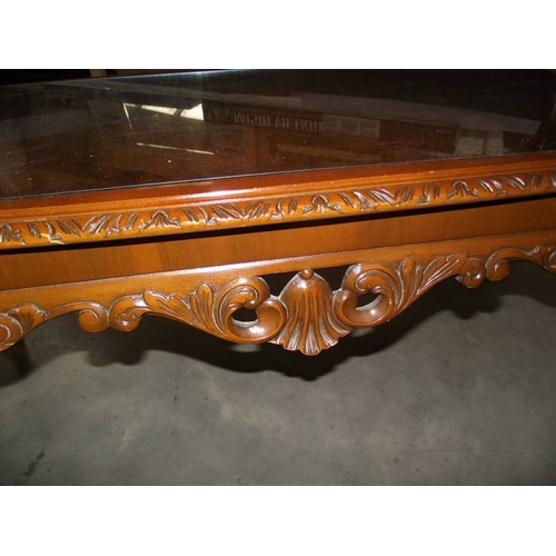 615 - A dark wood stained carved long coffee table with glass top.