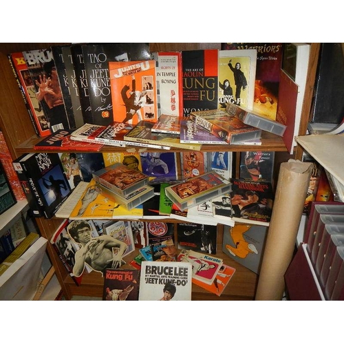 14 - Nine shelves of Bruce Lee related items, Kung Fu books. posters, videos etc.,