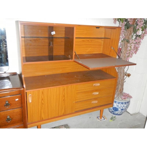 661 - A teak glazed sliding door cabinet with drop down side and three drawers.