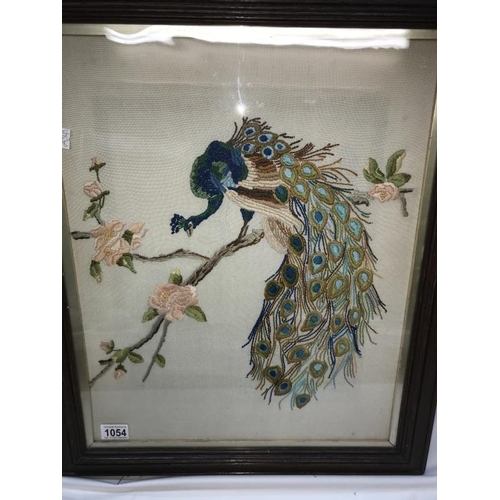 1054 - A framed & glazed embroidered picture of a Peacock.  (Collect only)