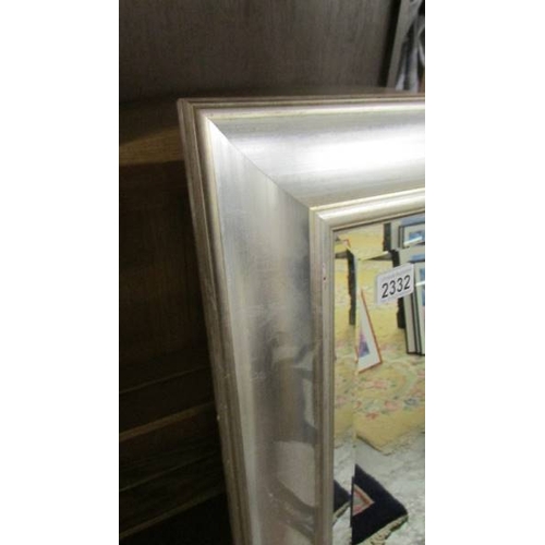 2332 - A large bevel edged mirror in silver coloured frame. 106 x 72 cm. (Collect only)