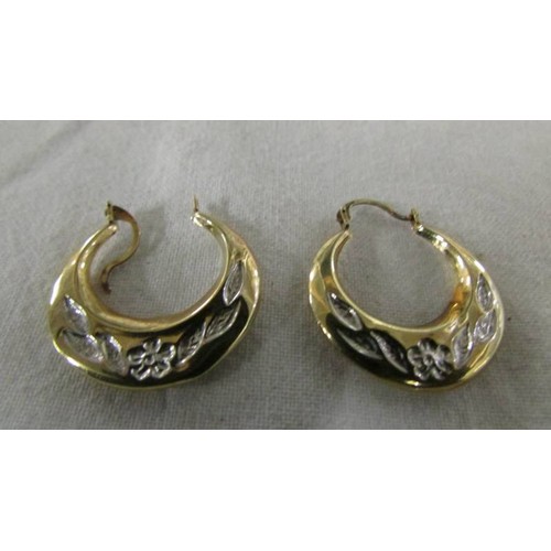 1067 - A pair of 9ct gold hoop earrings engraved with flowers and foliage.