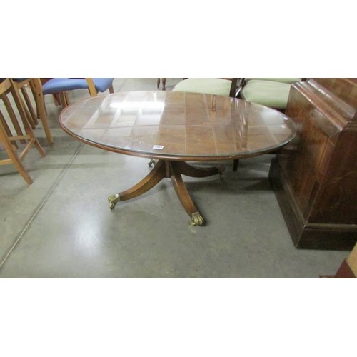 1585 - An oval coffee table with glass top on brass lion paw casters.