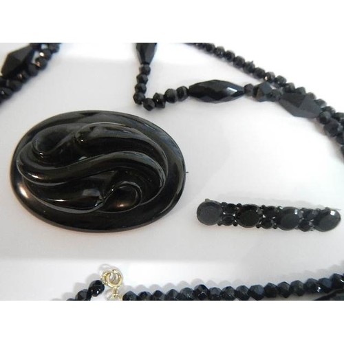 1137 - Two black Whitby jet style brooches and a black necklace.