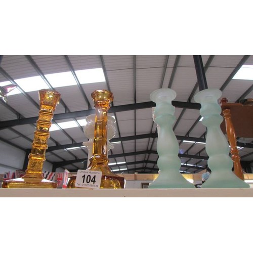 104 - Two amber coloured candlesticks, a pair of green glass candlesticks and 2 white candlesticks.