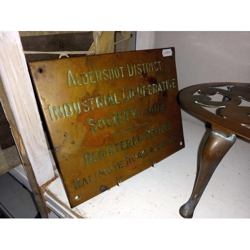 109 - A Brass Aldershot co-op sign and a large oval brass trivet.