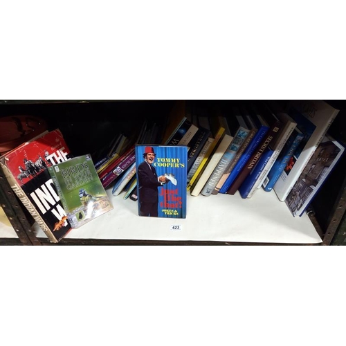 423 - A shelf of hard back & paper back books including Tommy Cooper etc.