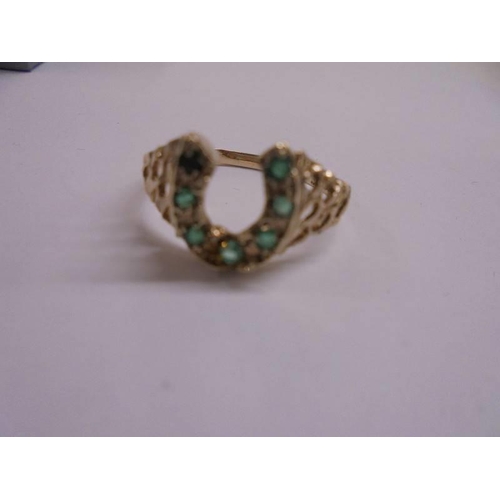 1048 - An unusual emerald set horse shoe ring dated London 1978 set with 7 emeralds in a textured openwork ... 