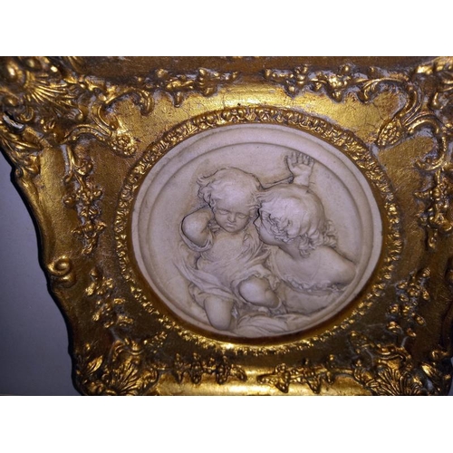 217 - An ornate gilt framed plaque of children, diameter 17cm, frame 29cm x 29cm