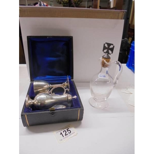 125 - A three piece cased silver Holy communion set and a glass ewer with silver topped cork.