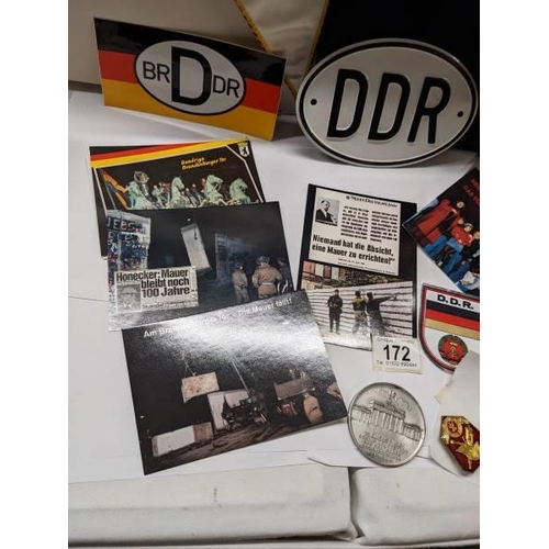 172 - A box of East German ephemera including flags, car badges, pin badges, medalliion and postcards.