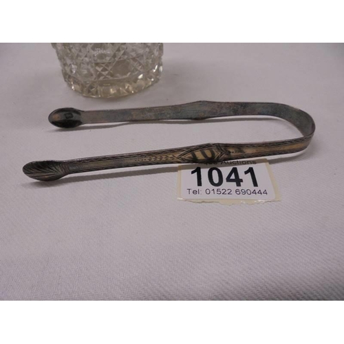 1041 - A glass hair pot with silver top and a pair of hall marked silver sugar tongs.