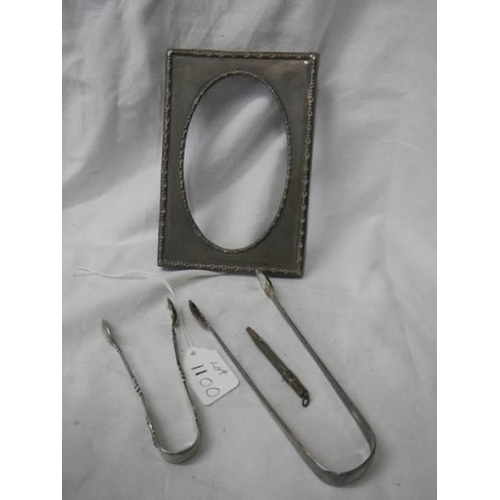 1100 - A silver photo frame, two silver sugar tongs and a silver pencil.